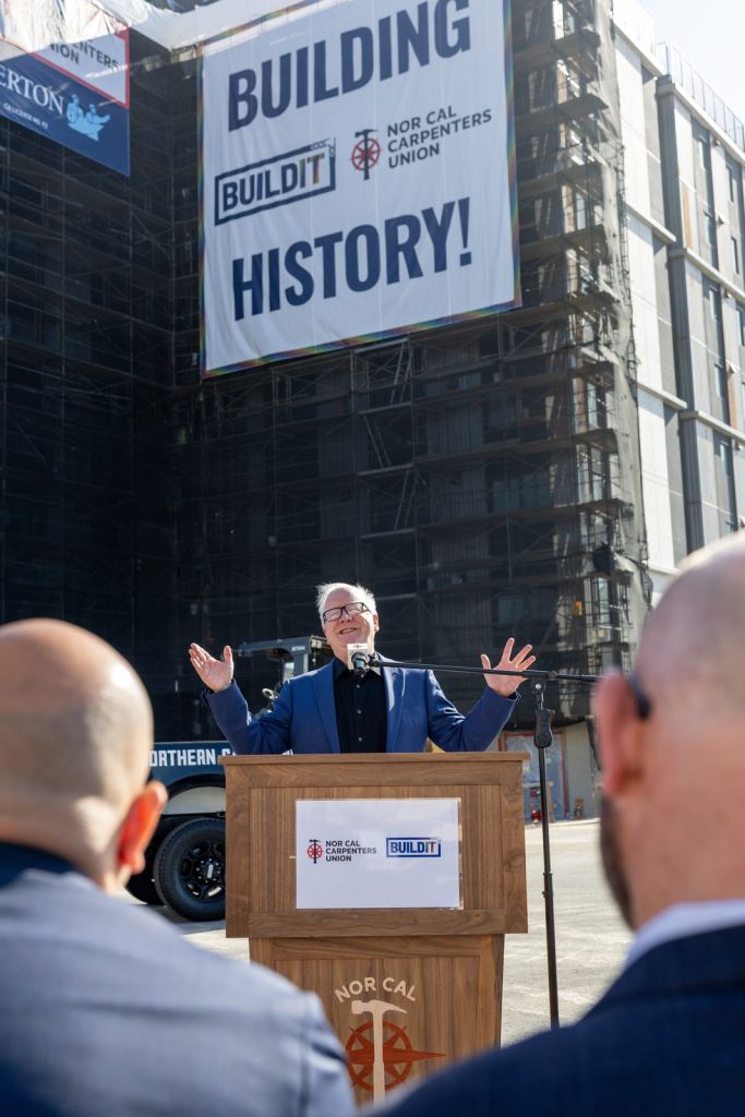 Speaker at a Nor Cal Carpenters podium beneath an oversized Building History banner