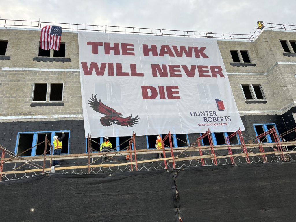 Crew under an oversized The Hawk Will Never Die banner on a Hunter Roberts building