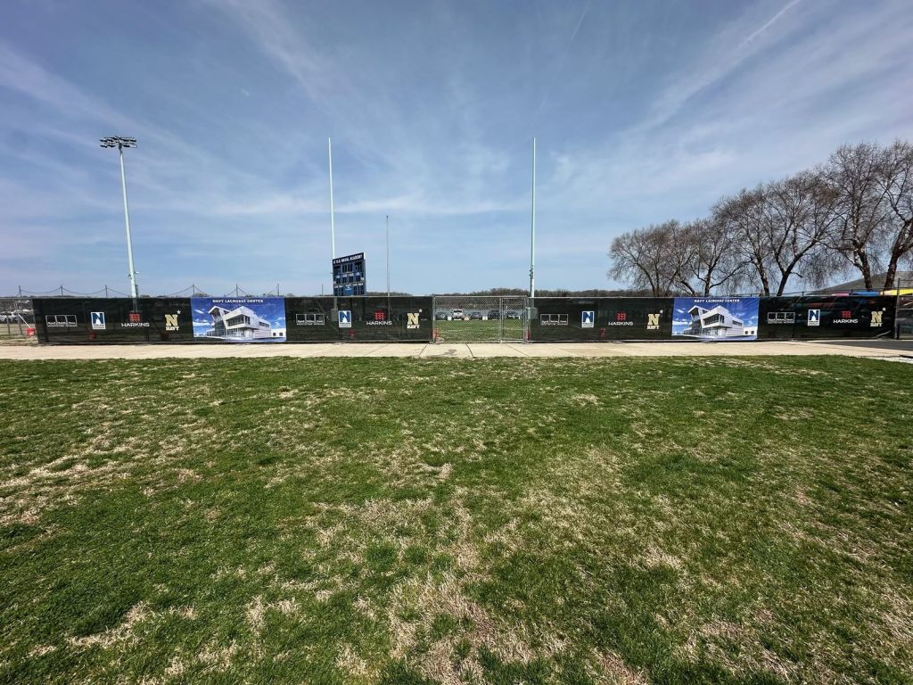 Full-color printed windscreens with Navy Lacrosse Center rendering and sponsor logos on a field fence